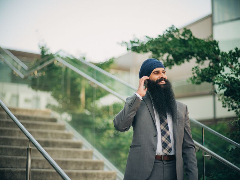 Smiling businessman with a beard and turban talks on phone outside on sunny day
