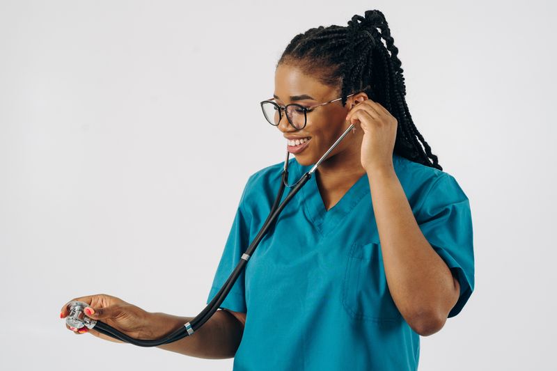 Female doctor in blue scrubs, smiling while holding a stethoscope