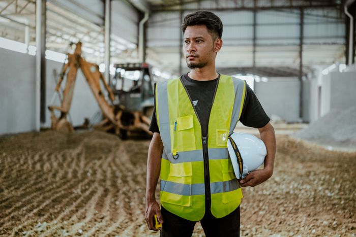 Portrait of a construction worker in safety gear holding a helmet
