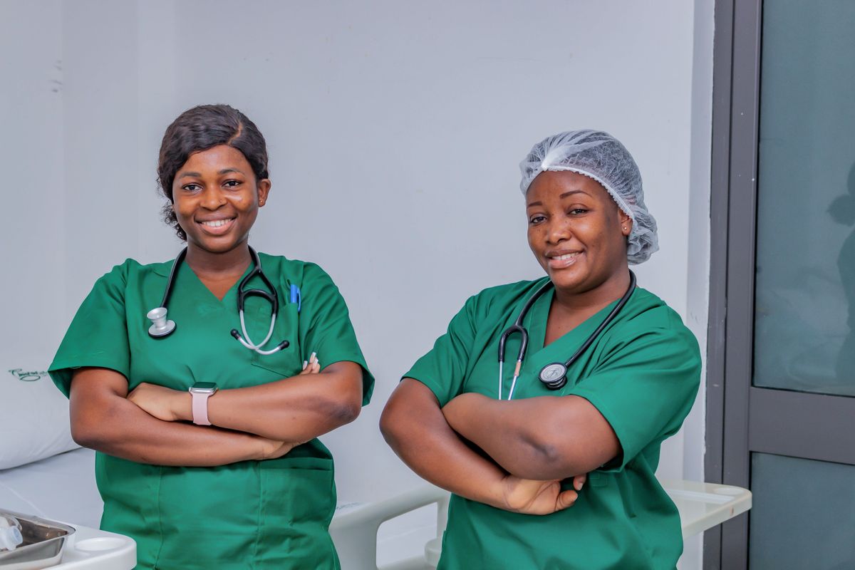 Two female nurses in green scrubs smiling confidently in a hospital room
