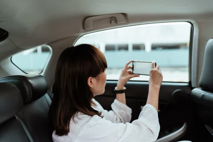 A woman in the back of a car taking a photo with her phone