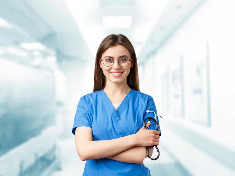 Young nurse in blue scrubs smiling and holding a stethoscope