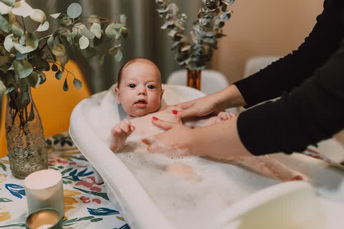 A parent bathing a baby in a small tub
