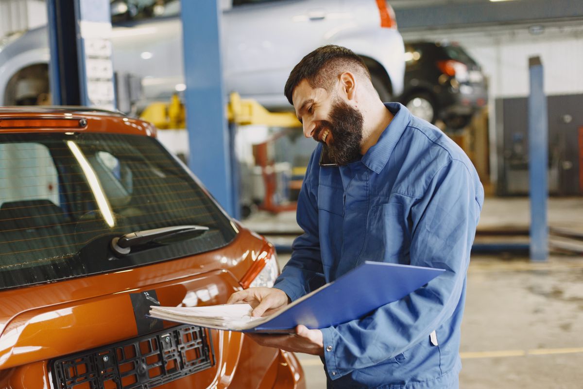 Smiling auto mechanic inspects a car