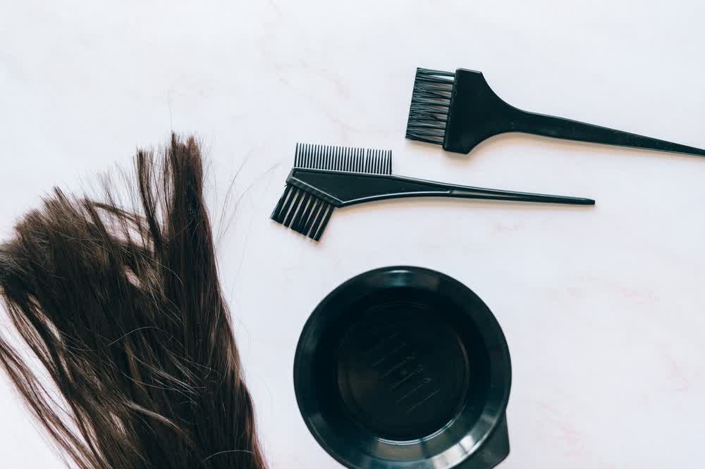Brushes and a bowl for applying a hair treatment, beside a lock of dark hair