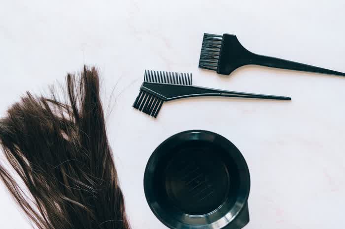 Brushes and a bowl for applying a hair treatment, beside a lock of dark hair