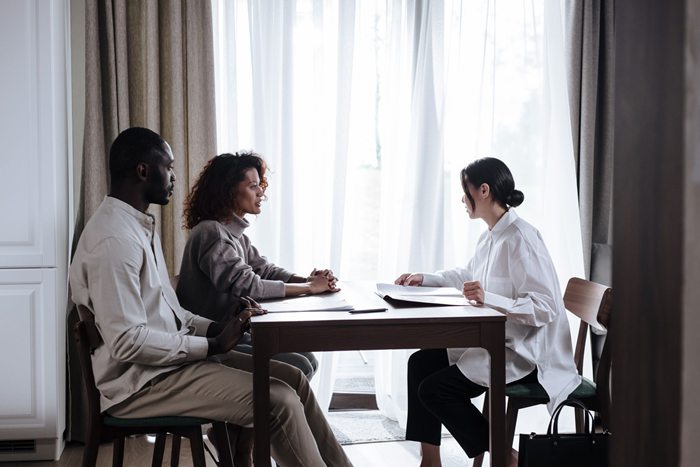 A woman in a white shirt smiling during a meeting with a couple indoors